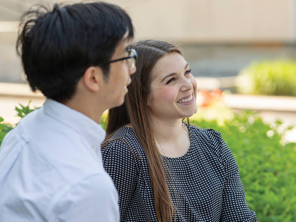 A man and woman in business attire sit outside.