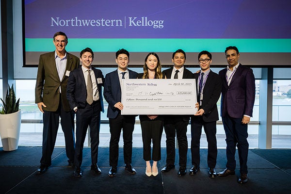 One older man standing next to 6 students in business attire holding novelty check for $15,000.