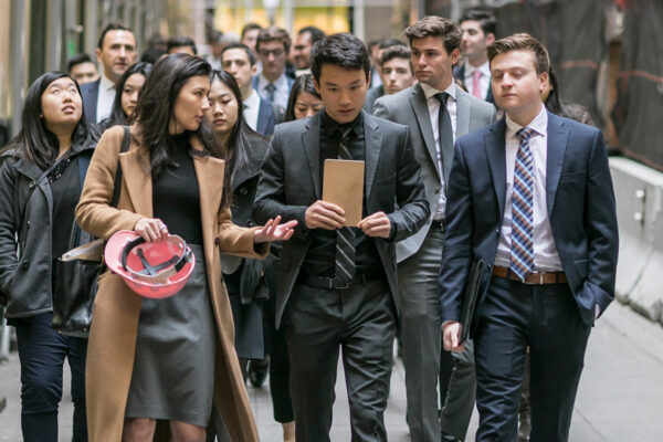 A group of students in business attire walk down a hallway.