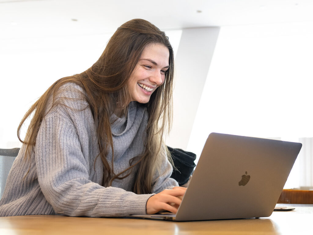 A woman smiles in front of a laptop.