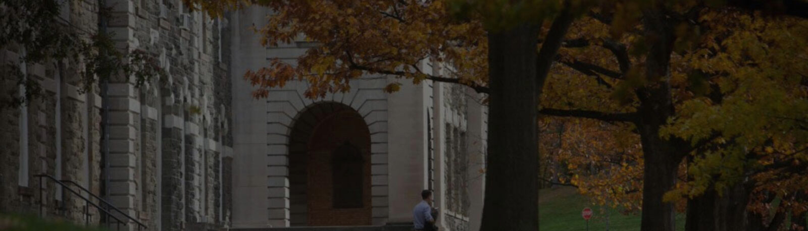 Man walking in front of a building on Cornell's campus in the fall.