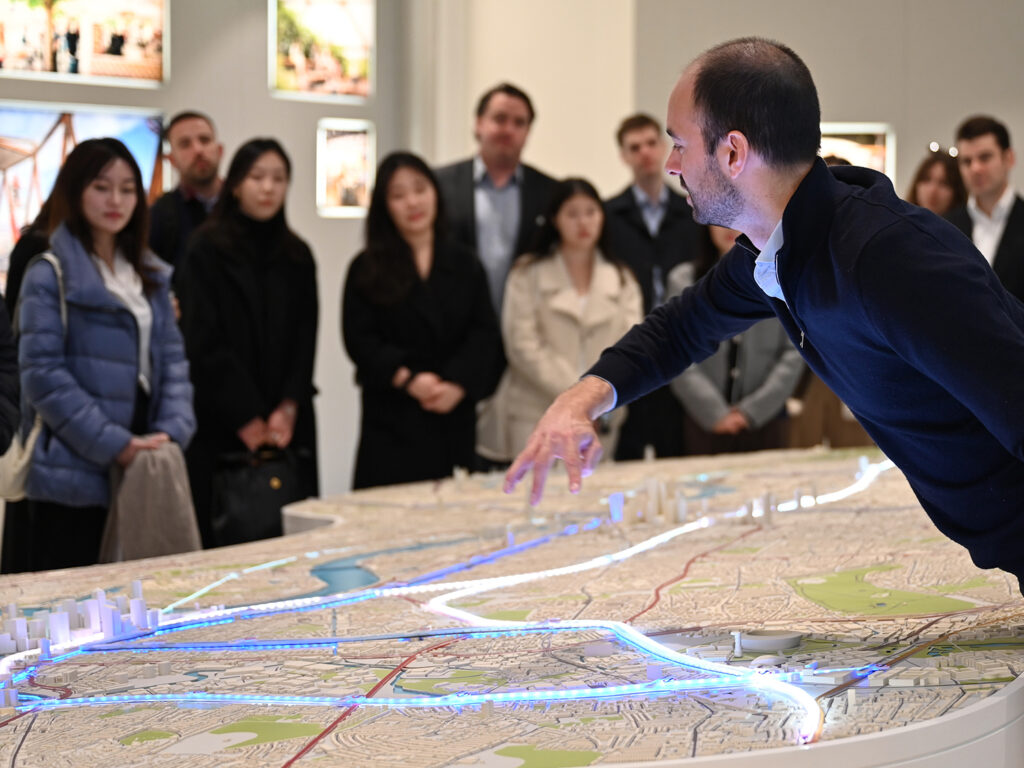 A man speaks and indicates with his hands over a map and model of a city..