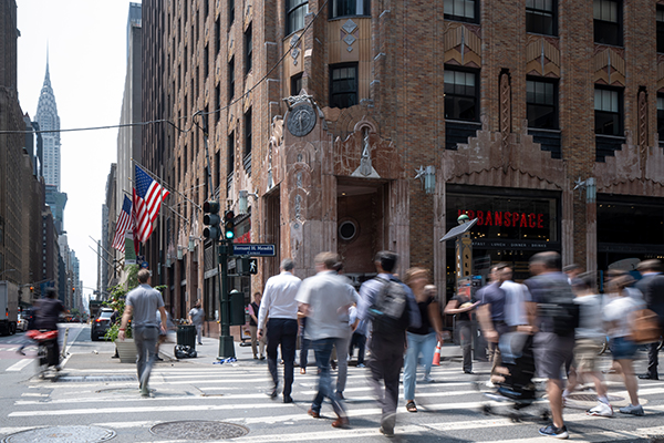 People walking across the street with 570 Lexington Ave in the background.