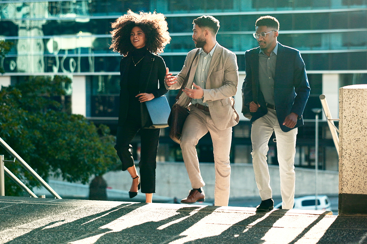 Three people in business attire walking up exterior stairs with the sun in the background.