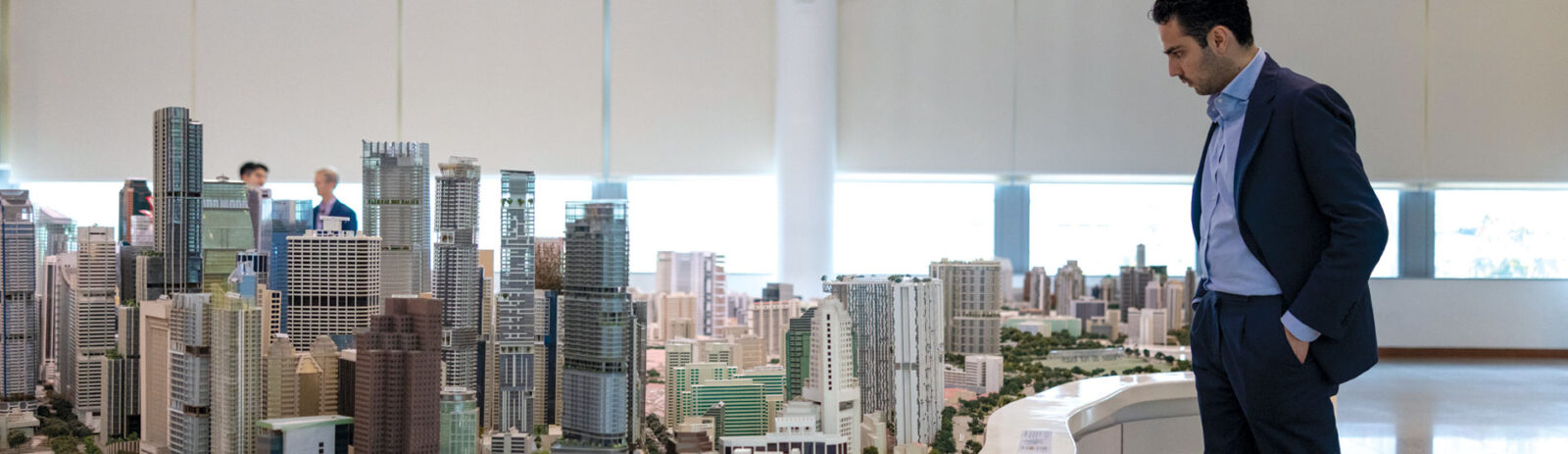 A man in a suit stands next to a large architectural model.