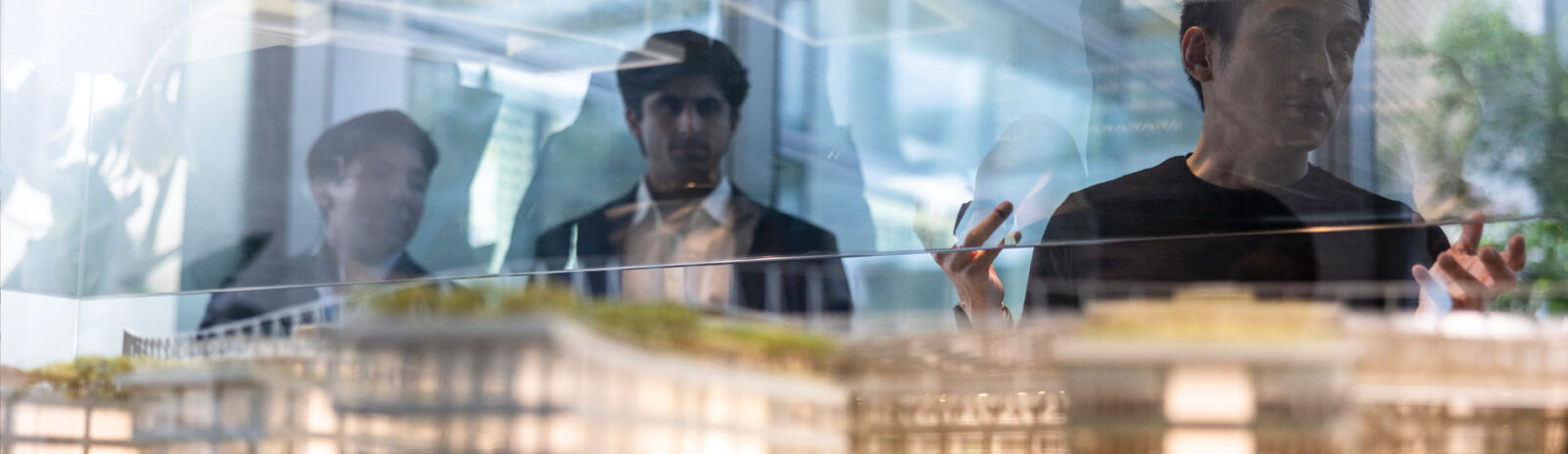 Three men in suits look over a architecture model.