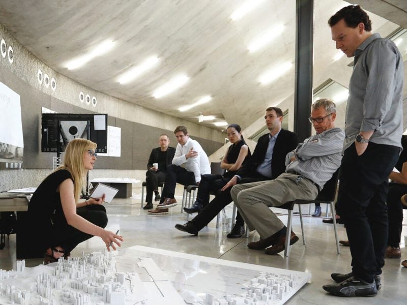 Woman leans in front of building model as others look on