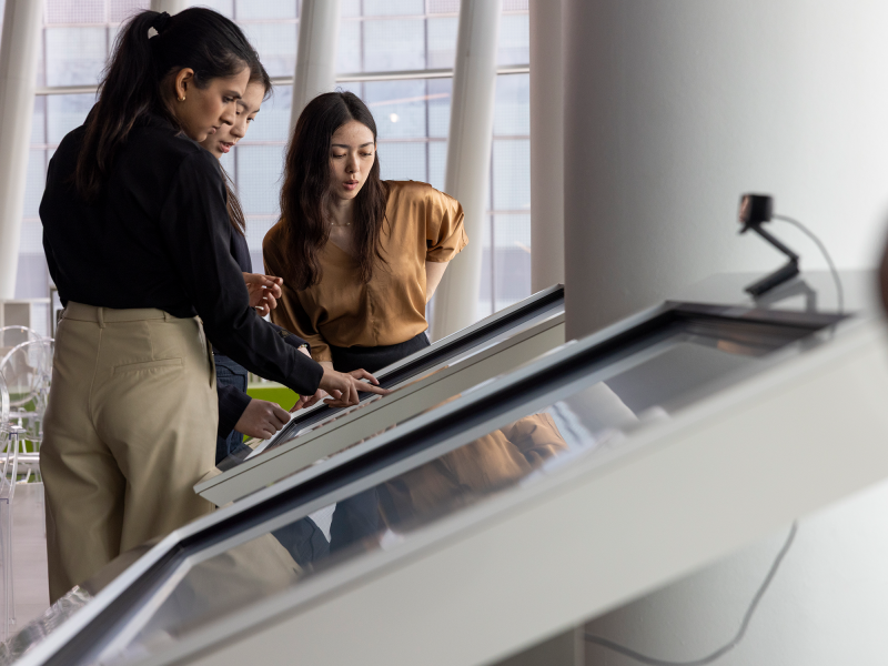 Three women students in the MPS-RE program review building designs on a display screen.