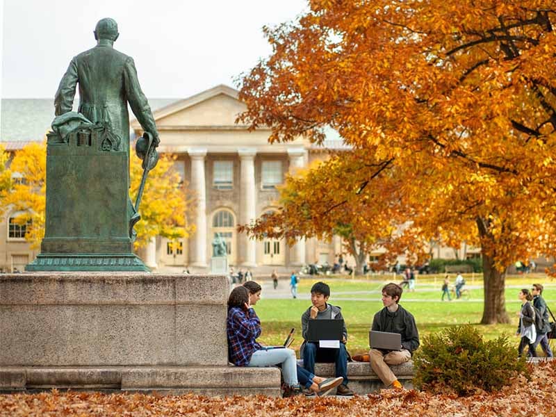 Students sitting near the Ezra Cornell statue on Cornell's Ithaca Campus on a fall day.